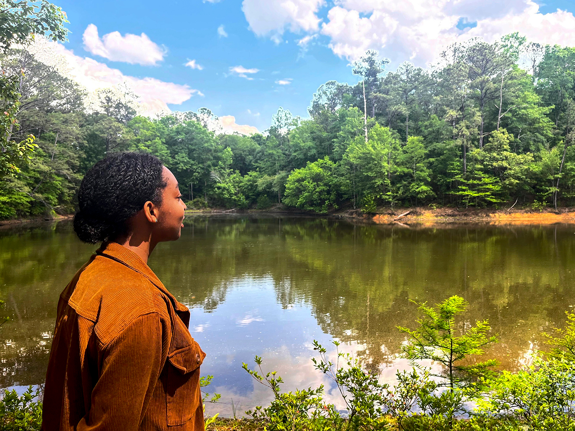A woman looks across a pond surrounded by trees.